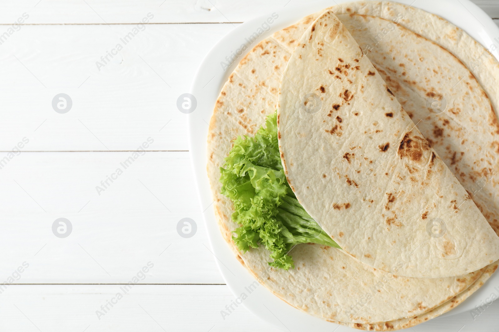 Photo of Tasty homemade tortillas and lettuce on white wooden table, top view. Space for text