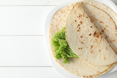 Tasty homemade tortillas and lettuce on white wooden table, top view. Space for text
