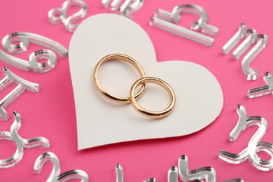 Photo of Zodiac signs, heart and wedding rings on pink background, closeup