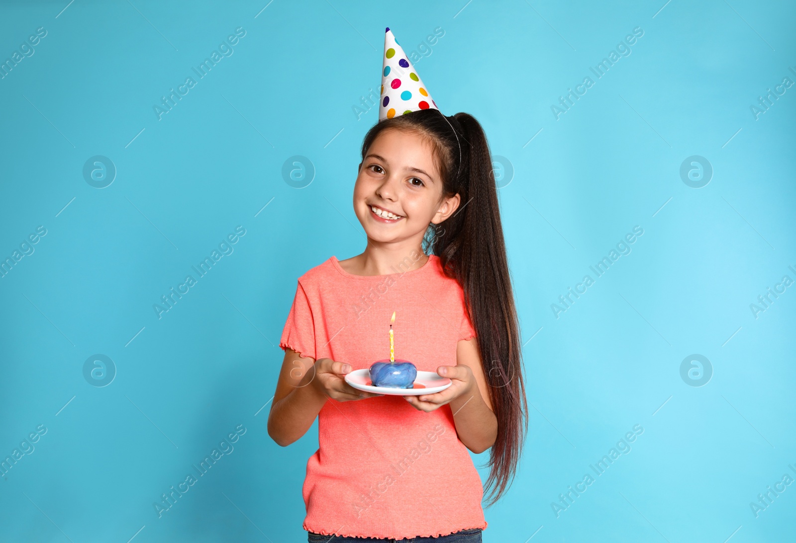 Photo of Happy girl holding birthday sweetness with candle on blue background