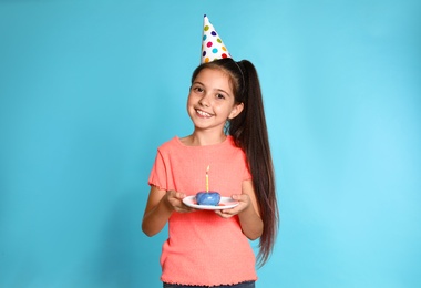 Happy girl holding birthday sweetness with candle on blue background