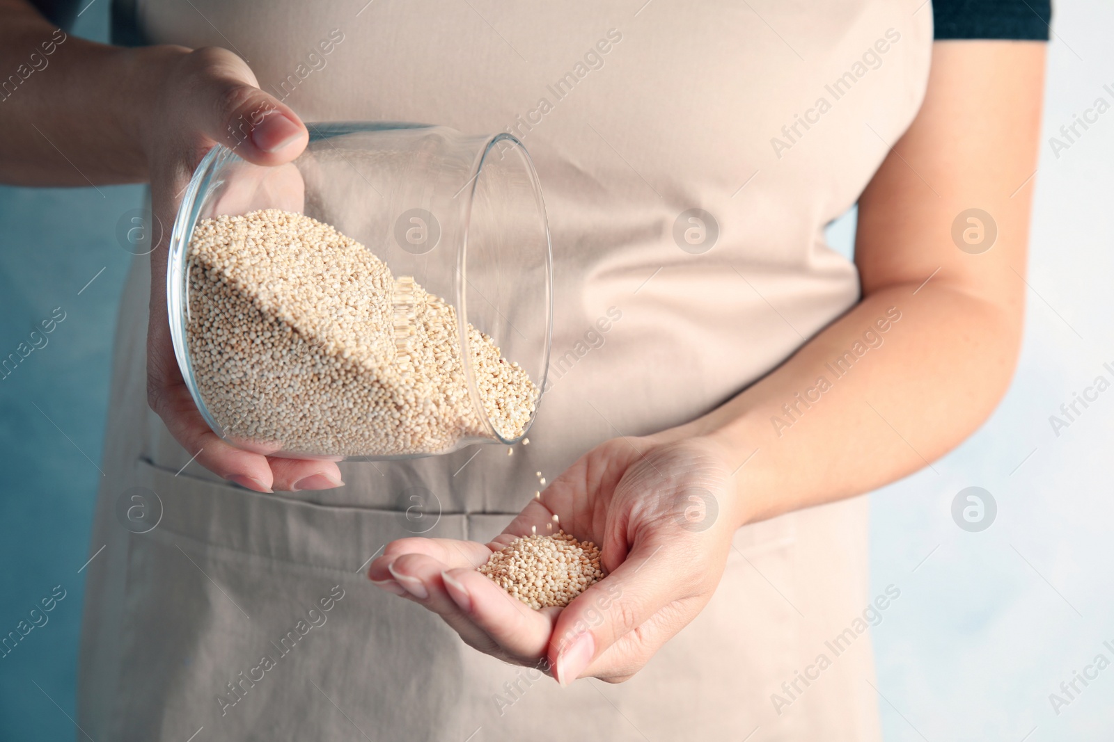 Photo of Woman pouring white quinoa from jar into hand on light background, closeup