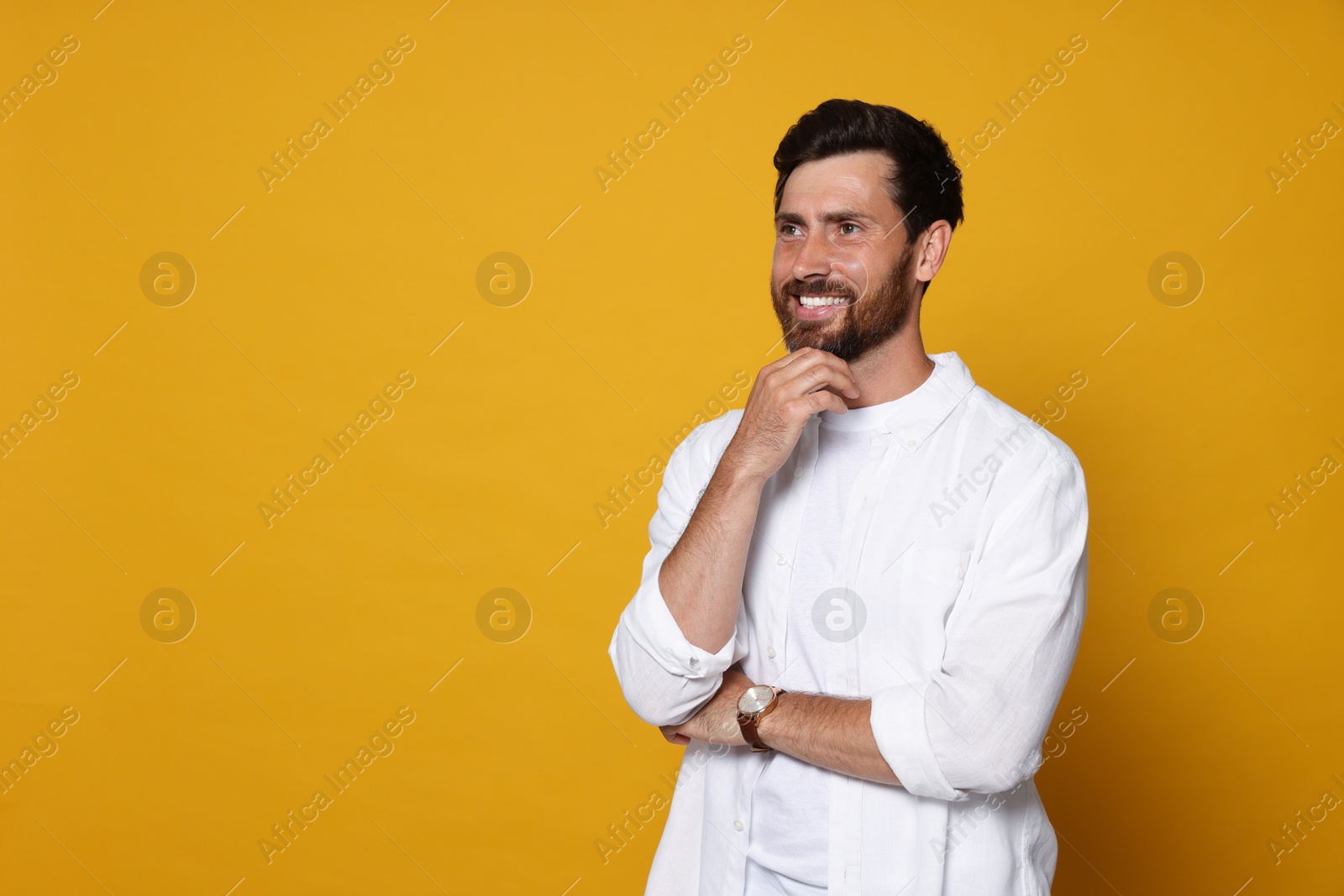 Photo of Portrait of smiling bearded man with wristwatch on orange background. Space for text