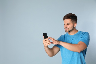 Photo of Young man with vision problems using smartphone on grey background, space for text