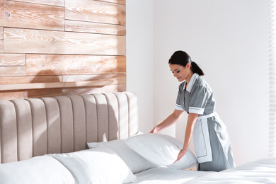 Photo of Young chambermaid making bed in hotel room. Space for text