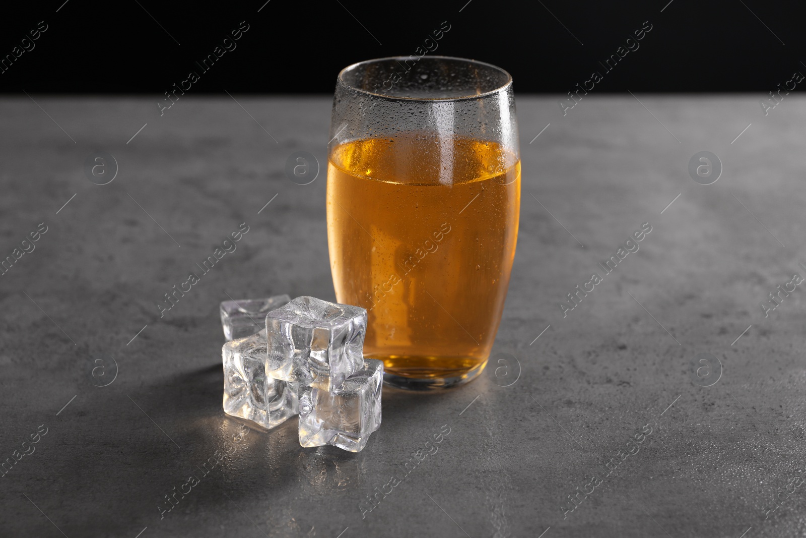 Photo of Energy drink in glass and ice cubes on grey table