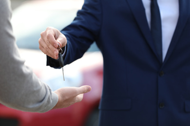 Photo of Salesman giving key to customer in modern auto dealership, closeup. Buying new car