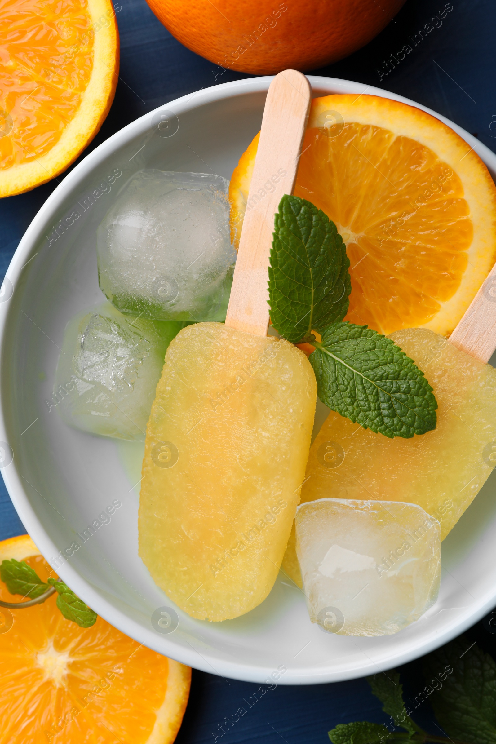 Photo of Tasty orange ice pops on blue wooden table, flat lay. Fruit popsicle