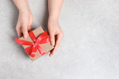 Photo of Woman holding gift box with red bow at light grey table, top view. Space for text