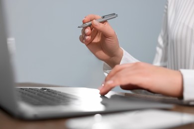 Woman with smartphone and pen working on laptop at wooden table, closeup. Electronic document management