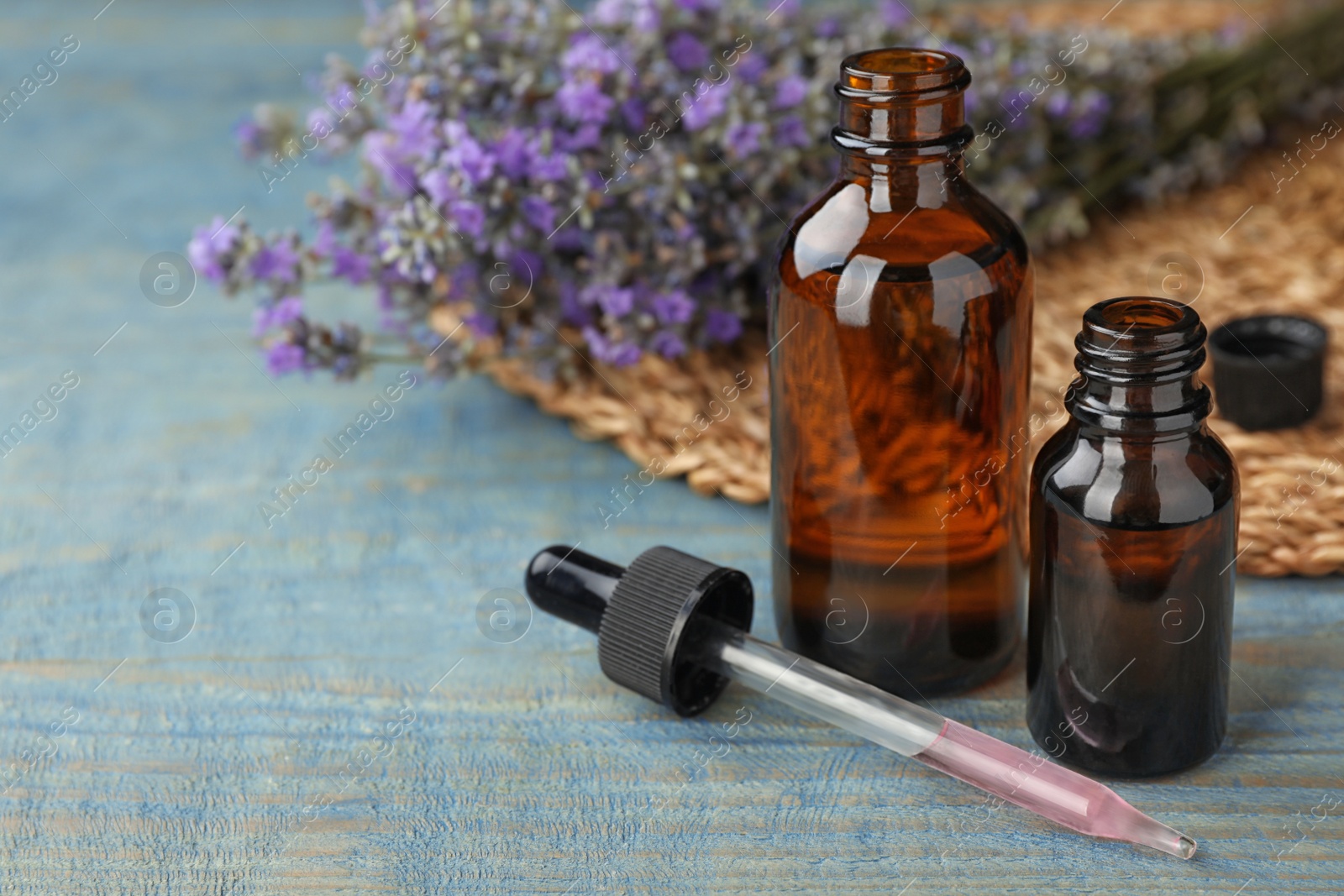 Photo of Bottles with natural lavender essential oil on blue wooden background. Space for text