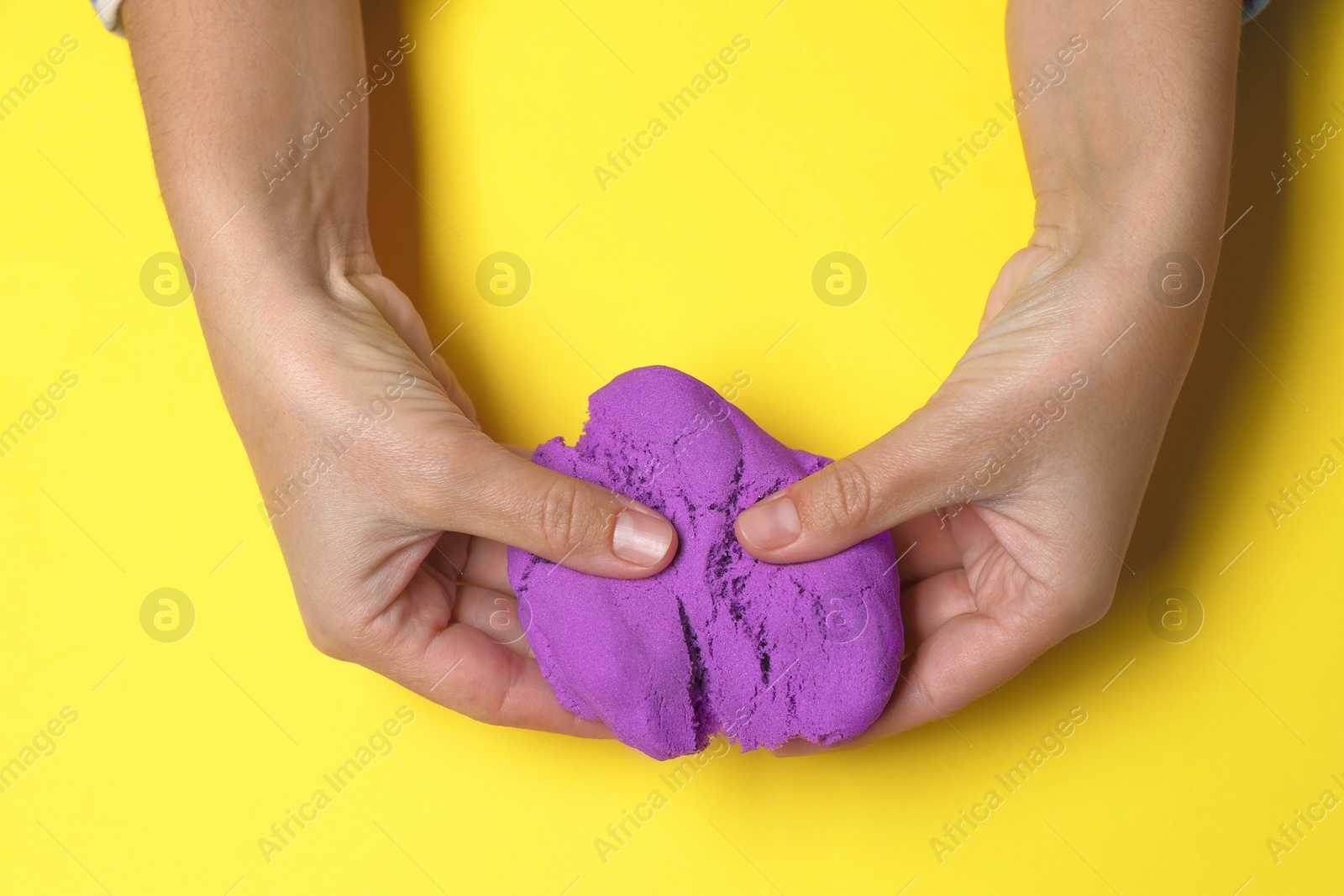 Photo of Woman playing with kinetic sand on yellow background, top view