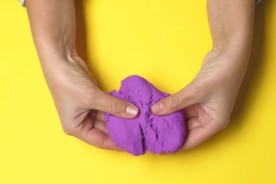 Woman playing with kinetic sand on yellow background, top view