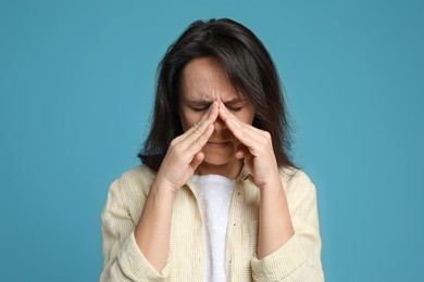 Mature woman suffering from headache on light blue background