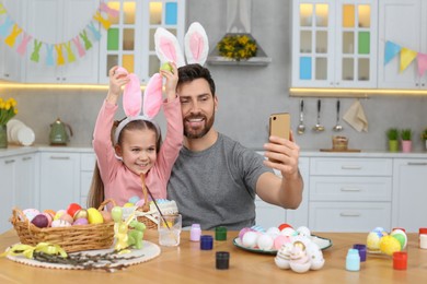Photo of Father with his cute daughter making selfie at table in kitchen. Painting Easter eggs