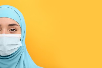 Photo of Muslim woman in hijab and medical mask on orange background, space for text
