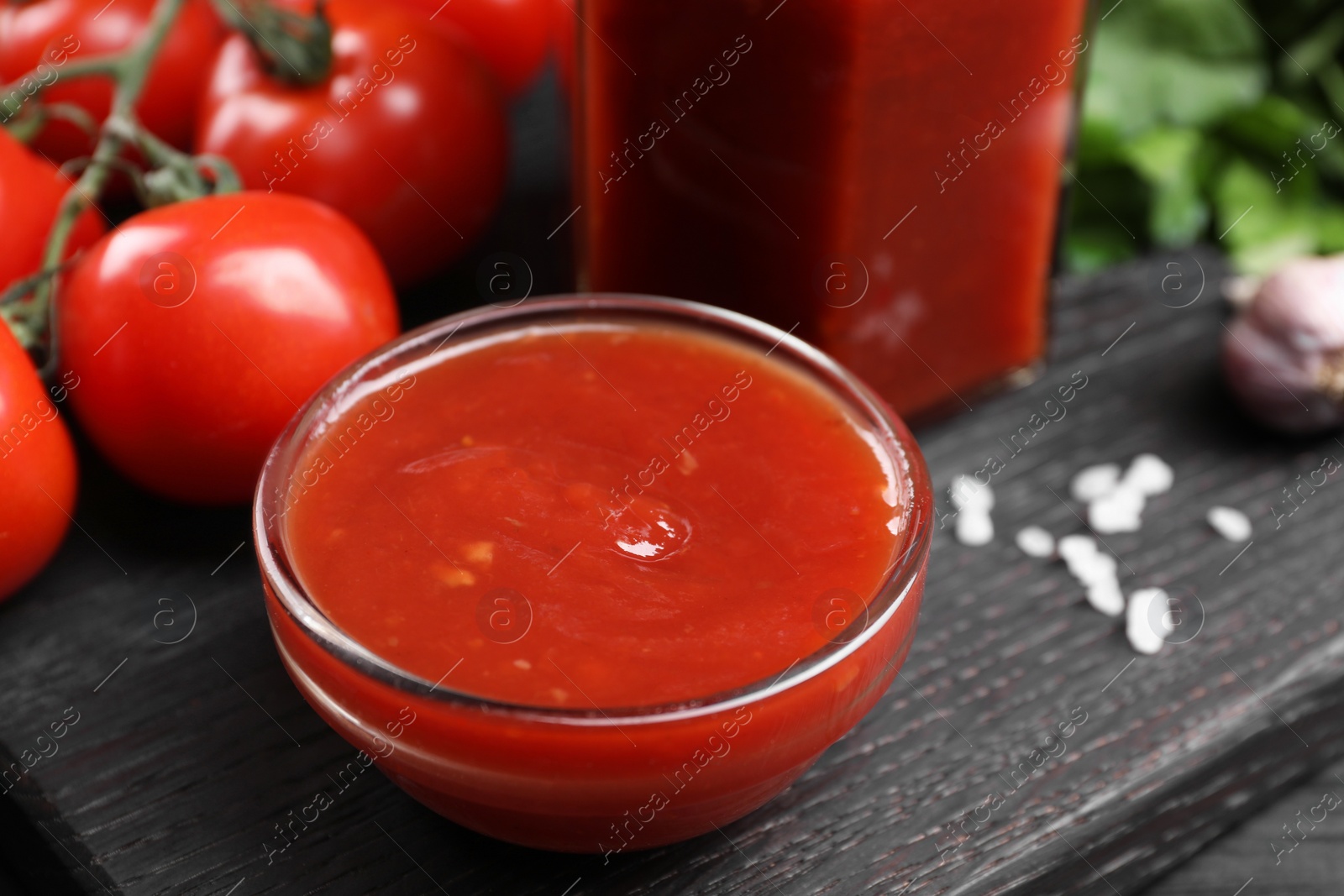 Photo of Delicious ketchup in bowl on black wooden table, closeup. Tomato sauce