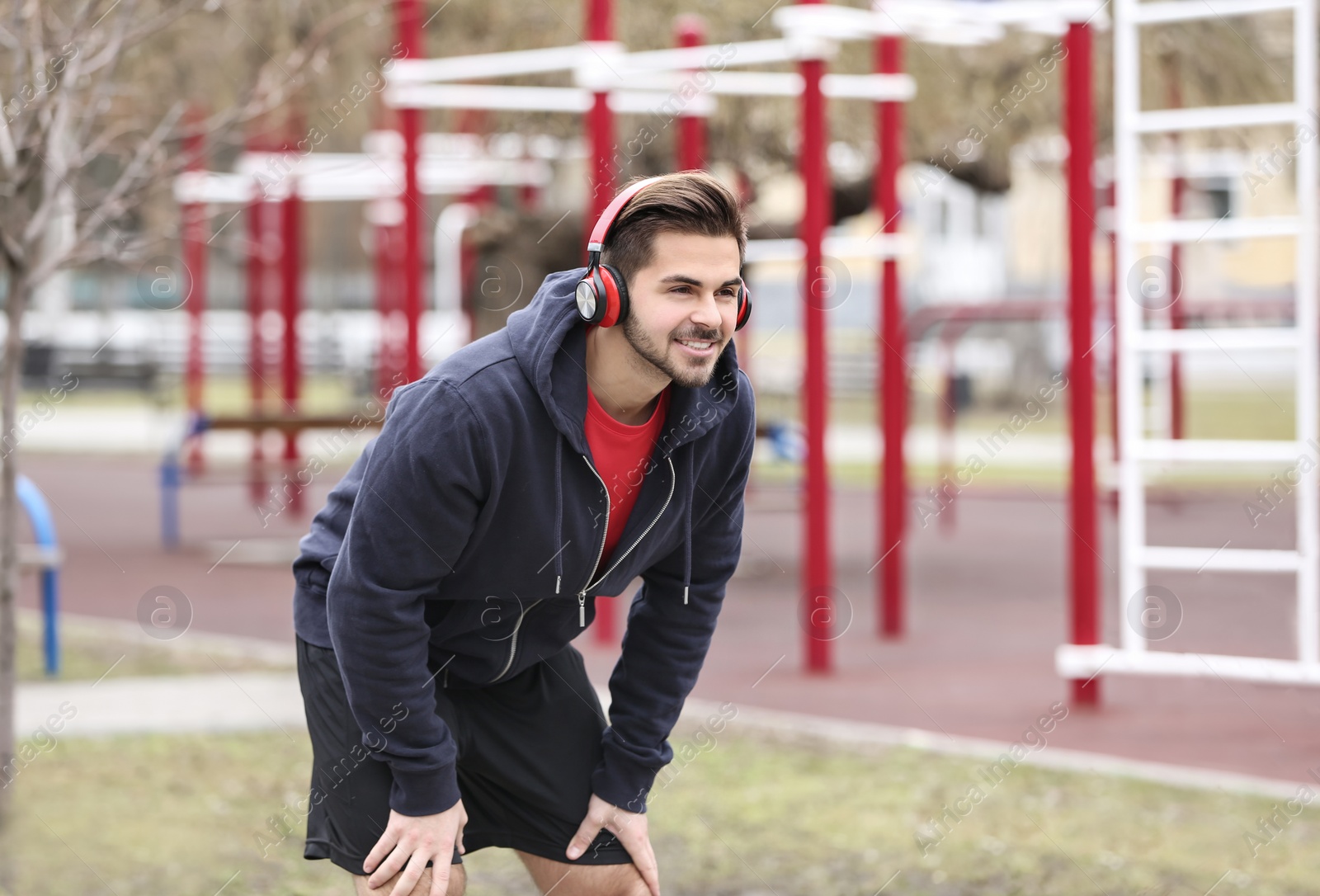 Photo of Young man with headphones listening to music and exercising on sports ground