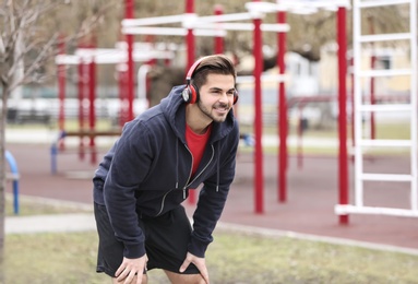 Young man with headphones listening to music and exercising on sports ground