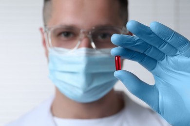 Doctor holding pill on light background, selective focus. Space for text