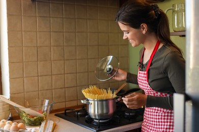 Photo of Young woman cooking spaghetti on stove in kitchen