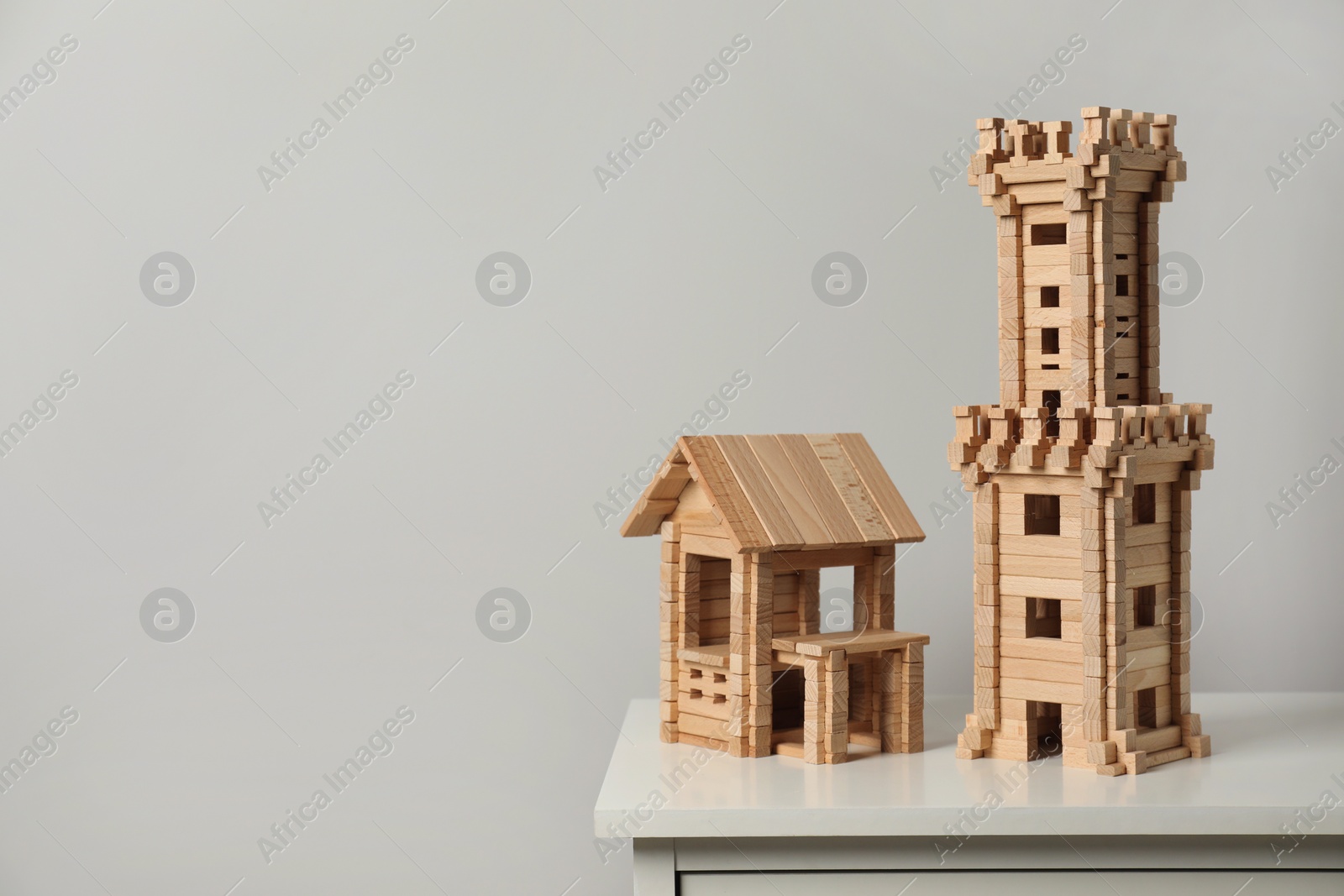 Photo of Wooden tower and house on chest of drawers near light grey wall, space for text. Children's toys