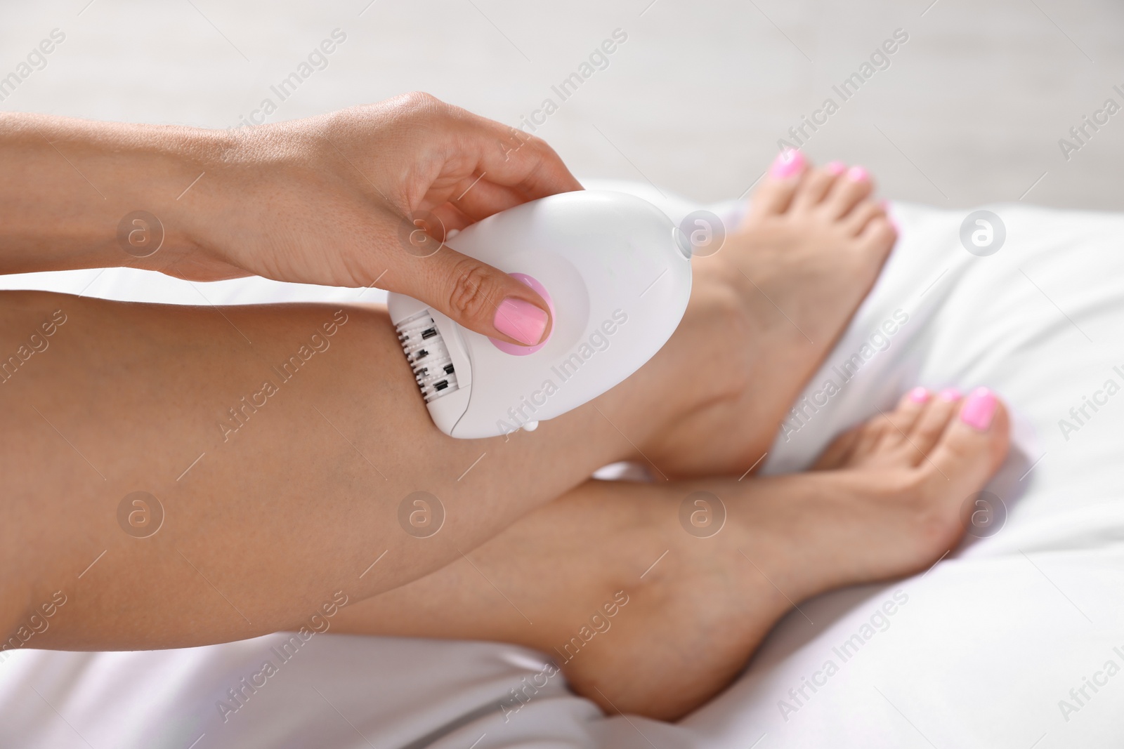 Photo of Young woman epilating her legs on bed, closeup