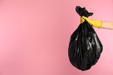 Photo of Janitor in rubber glove holding trash bag full of garbage on pink background, closeup. Space for text