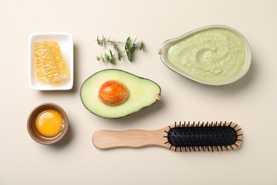Photo of Homemade hair mask in bowl, fresh ingredients and wooden brush on beige background, flat lay