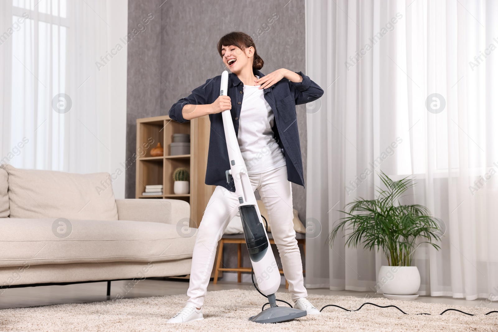 Photo of Happy young housewife having fun while cleaning carpet at home