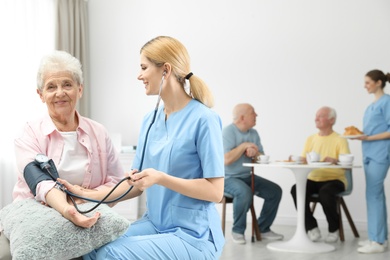Photo of Nurse measuring blood pressure of elderly woman at retirement home. Assisting senior people