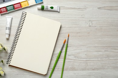 Flat lay composition with blank sketchbook on white wooden table. Space for text