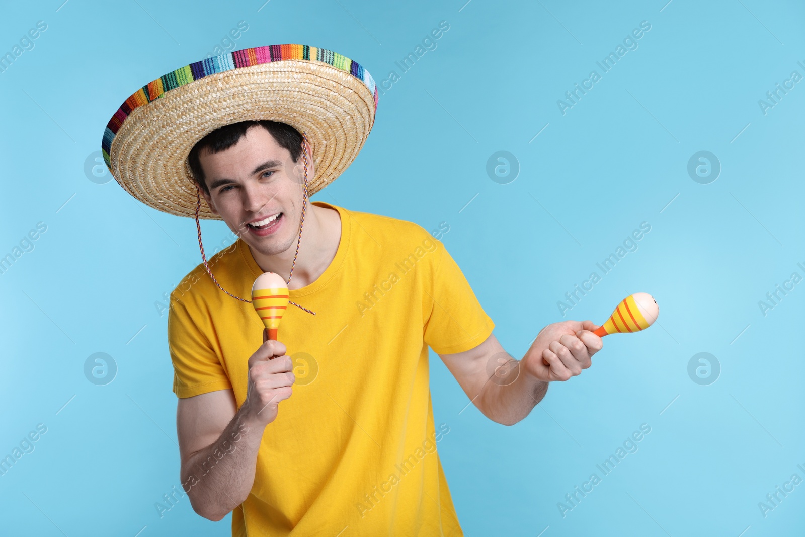 Photo of Young man in Mexican sombrero hat with maracas on light blue background