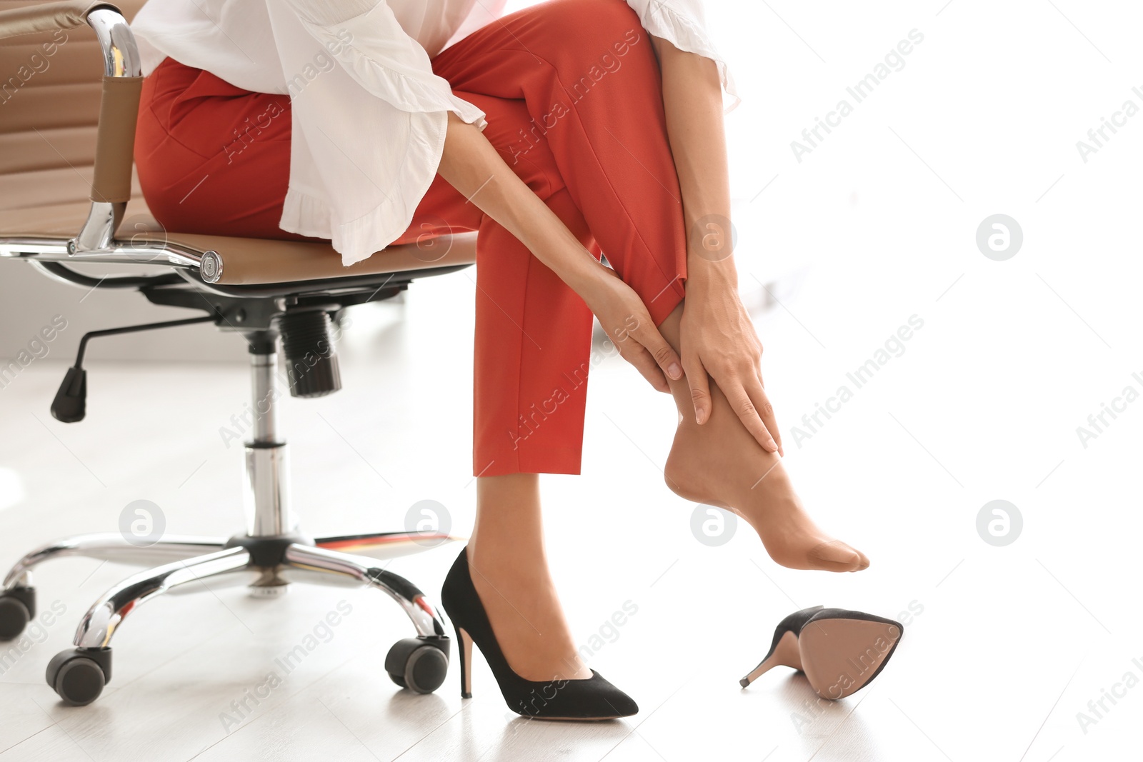 Photo of Tired woman taking off shoes at office, closeup view