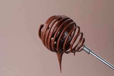 Chocolate cream flowing from whisk on light background, closeup
