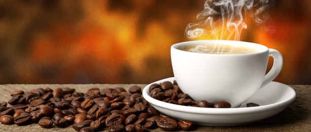 Cup of hot aromatic coffee and roasted beans on wooden table against color background. Banner design