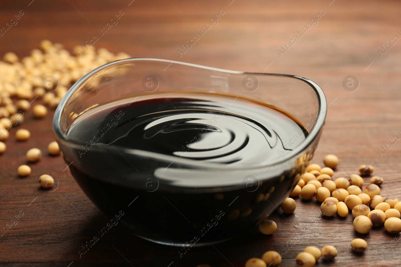 Photo of Soy sauce in bowl and soybeans on wooden table