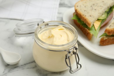 Jar of delicious mayonnaise near fresh sandwiches on white marble table