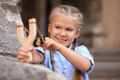 Photo of Cute little girl playing with slingshot outdoors