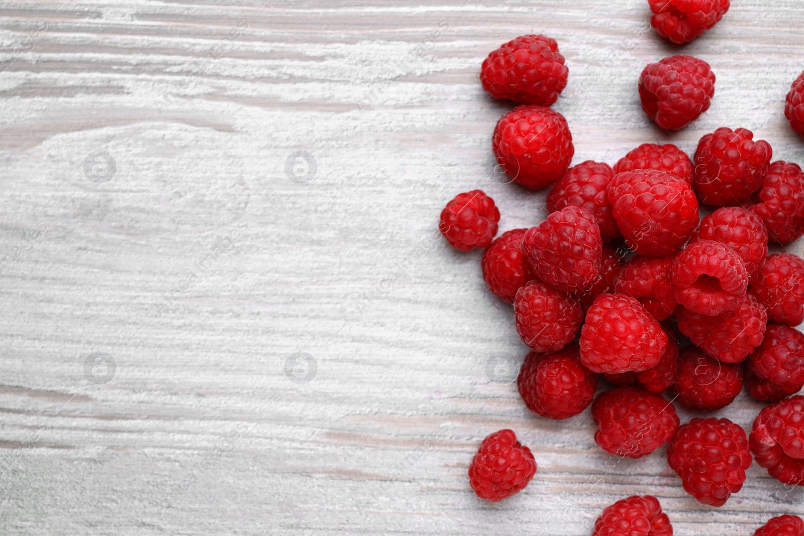 Photo of Tasty ripe raspberries on white wooden table, flat lay. Space for text