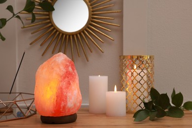 Photo of Himalayan salt lamp, candles and crystals on wooden table near white wall indoors