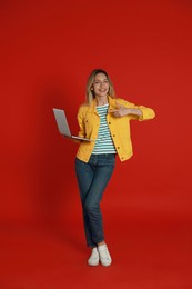 Young woman with modern laptop on red background