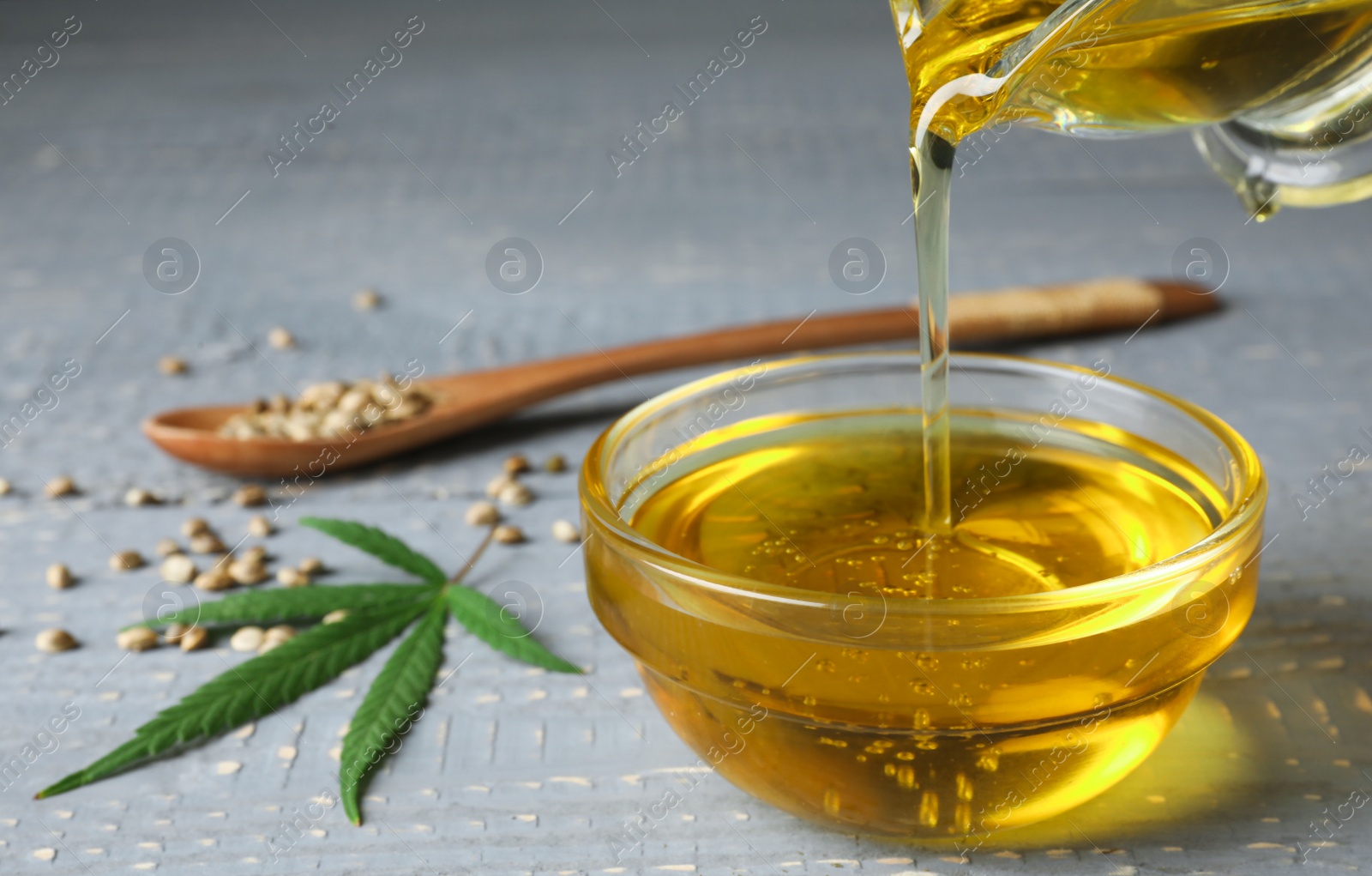 Photo of Hemp oil pouring from sauce boat into bowl on table