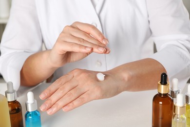 Photo of Dermatologist testing cosmetic product at white table, closeup