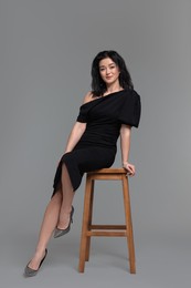 Beautiful woman in dress on stool against grey background