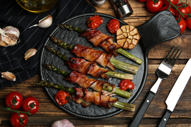 Photo of Oven baked asparagus wrapped with bacon on wooden table, flat lay