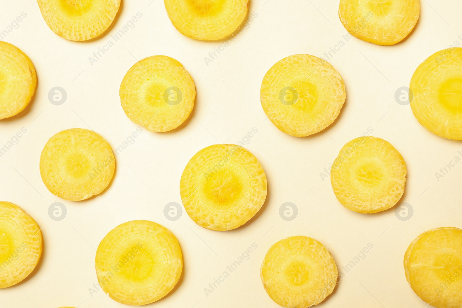 Photo of Slices of raw yellow carrot on beige background, flat lay