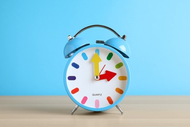 Photo of Alarm clock on white wooden table against light blue background