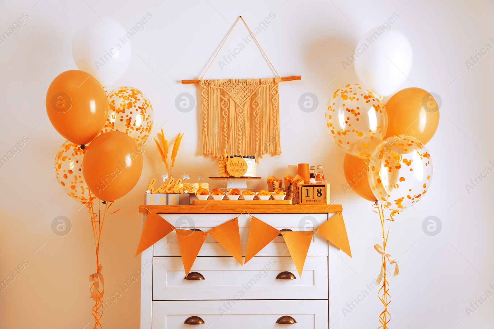 Image of Baby shower party. Different delicious treats on white wooden chest of drawers and decor near light wall