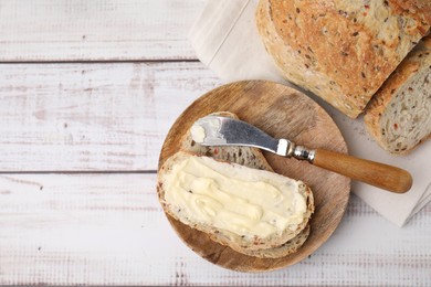 Photo of Tasty bread with butter and knife on white wooden table, flat lay. Space for text